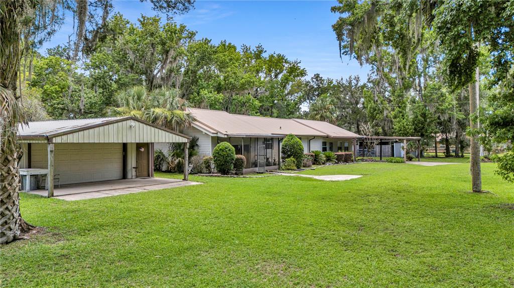 A single-story house with a metal roof, a detached carport, and a large grassy yard — 22308 BLUE CREEK LODGE ROAD, ASTOR, FL