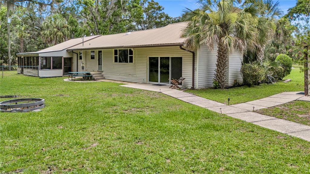 The exterior of a single-story house with a metal roof, screened porch, and concrete patio — 22308 BLUE CREEK LODGE ROAD, ASTOR, FL