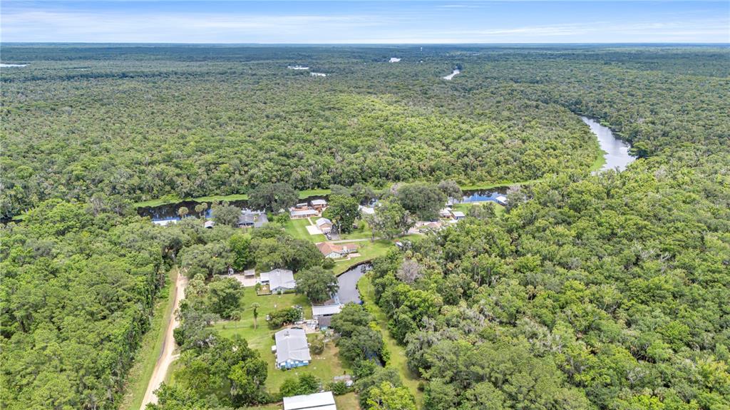 An aerial view shows several houses situated along a winding river surrounded by dense forest — 22308 BLUE CREEK LODGE ROAD, ASTOR, FL