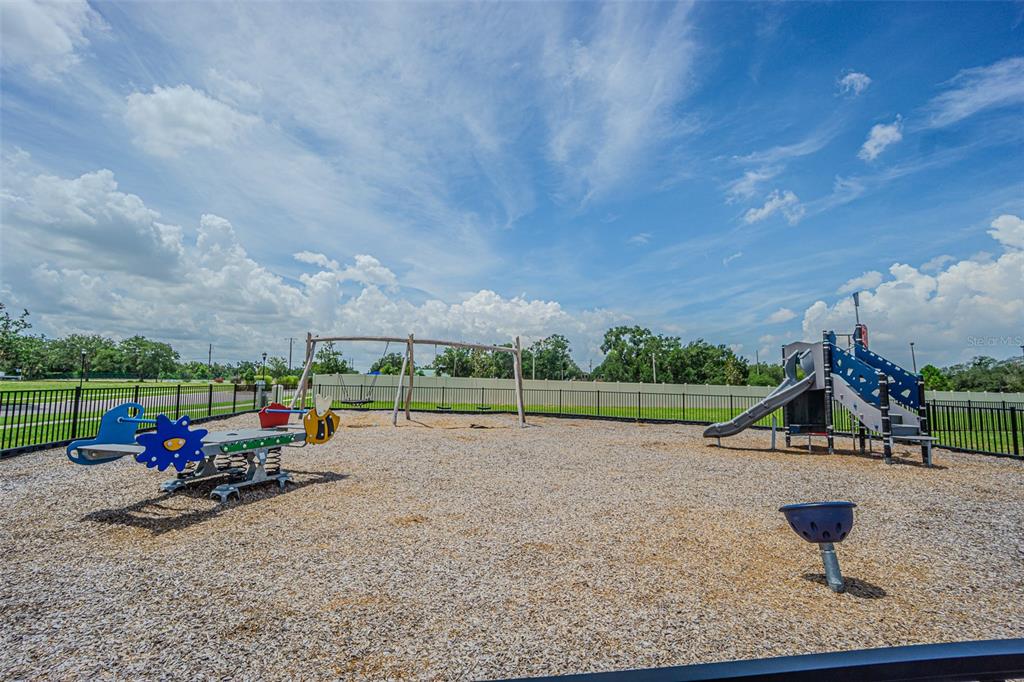 A fenced playground features a seesaw, a swing set, and a slide on wood chips — 9213 MISSION BAY PL, TEMPLE TERRACE, FL