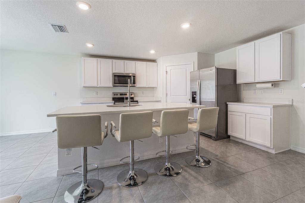 A kitchen features white cabinets, stainless steel appliances, a center island, and four bar stools — 9213 MISSION BAY PL, TEMPLE TERRACE, FL