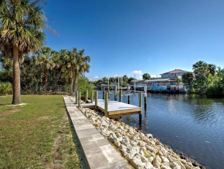 A wooden boat dock extends into a canal lined with a stone seawall and palm trees — 4342 EWING CIRCLE, PORT CHARLOTTE, FL