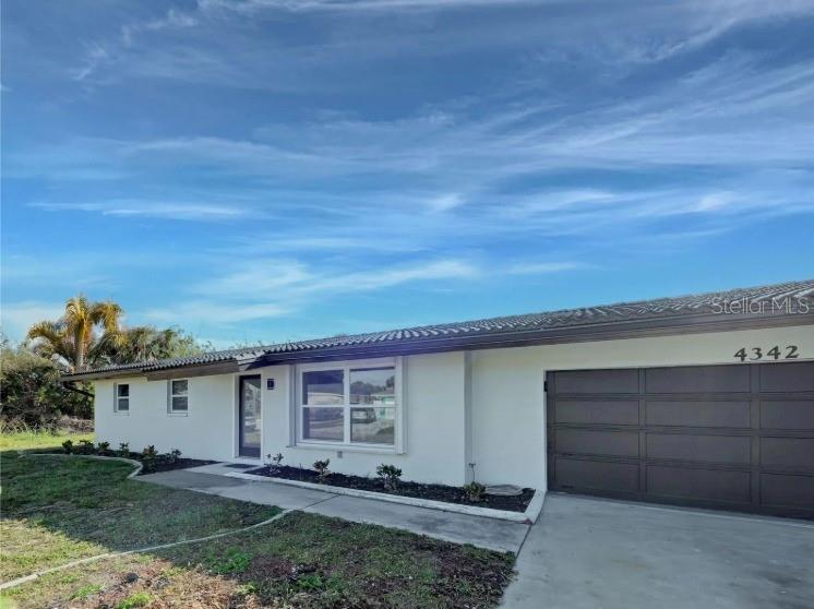 A single-story house with a white exterior, a dark garage door, and a tiled roof — 4342 EWING CIRCLE, PORT CHARLOTTE, FL
