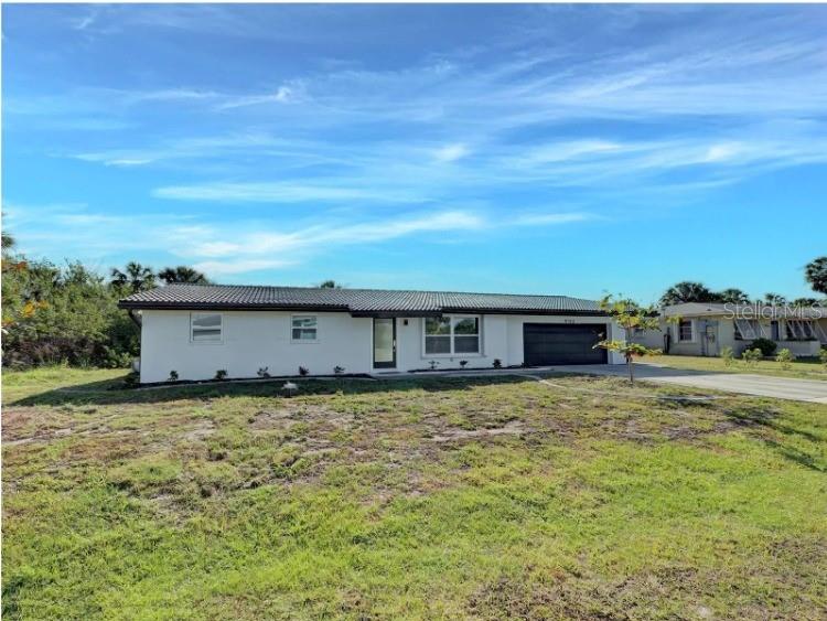 A single-story white house with a dark roof and garage sits on a grassy lot — 4342 EWING CIRCLE, PORT CHARLOTTE, FL