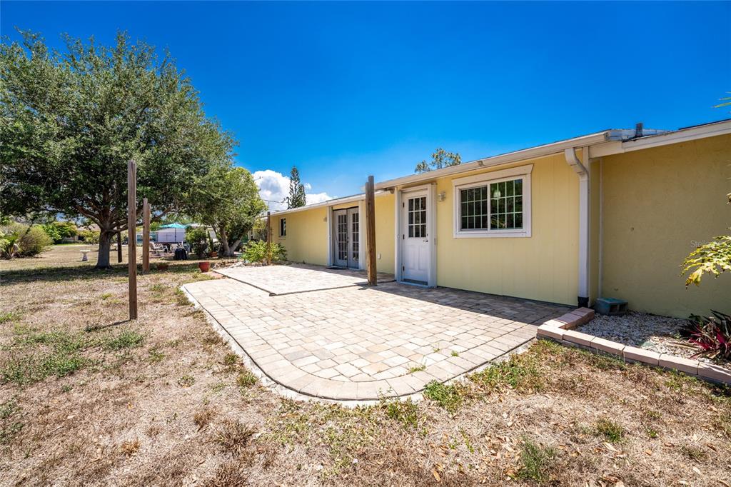 A yellow house exterior features a paved patio, a white door, and a large tree — 650 LEACH STREET, ENGLEWOOD, FL