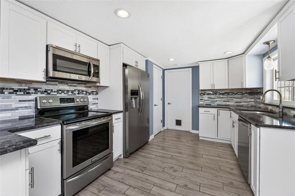 A kitchen with white cabinets, stainless steel appliances, dark countertops, and gray wood-look tile flooring — 650 LEACH STREET, ENGLEWOOD, FL