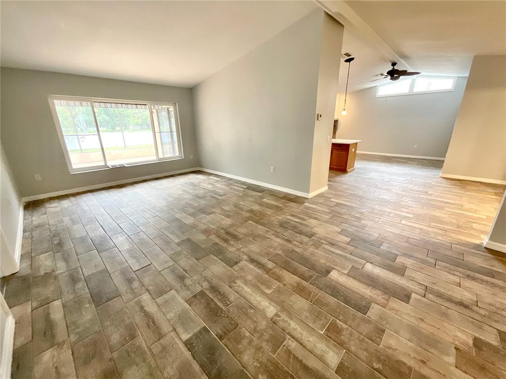 An open-concept living area features wood-look tile flooring, gray walls, and a large window — 2991 VALENCIA LANE E, PALM HARBOR, FL