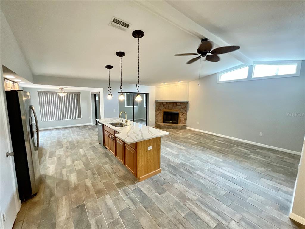 An open-concept kitchen and living area features wood-look tile flooring, a stone fireplace, and island — 2991 VALENCIA LANE E, PALM HARBOR, FL