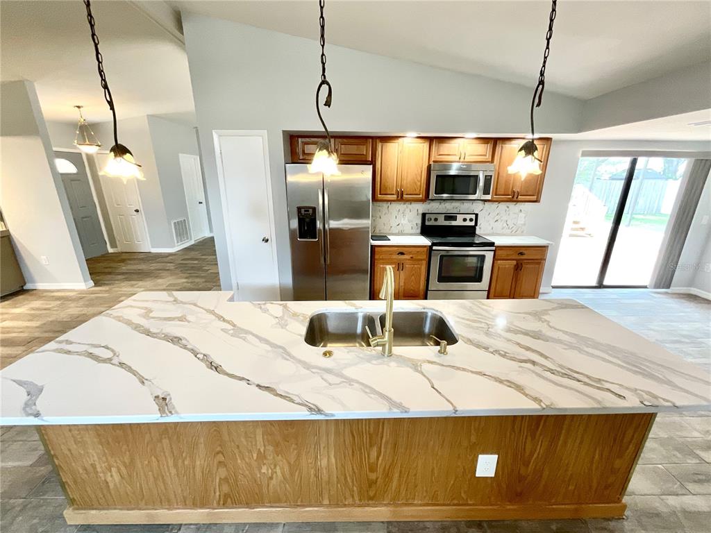 A kitchen features a large marble-topped island, wooden cabinetry, and stainless steel appliances — 2991 VALENCIA LANE E, PALM HARBOR, FL