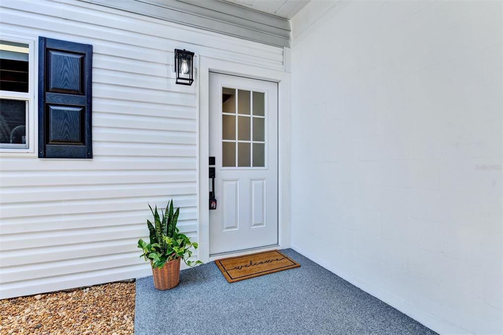 A white front door with a window sits on a porch next to a plant — 11906 DIETZ DRIVE UNIT 22, TAMPA, FL