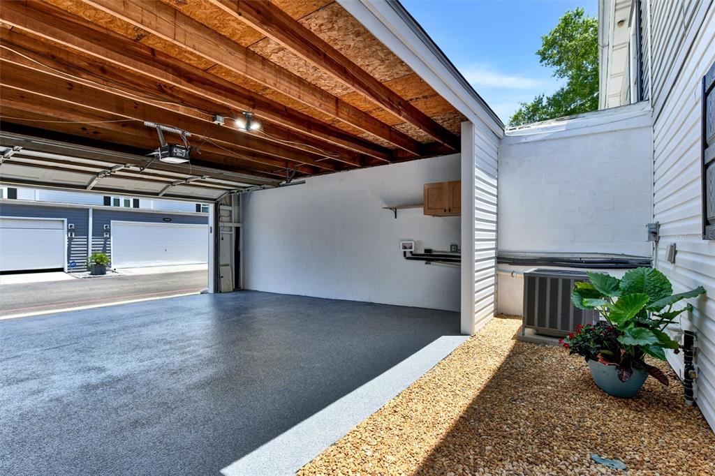 An open-air carport with a concrete floor, exposed wooden ceiling beams, and an adjacent gravel area — 11906 DIETZ DRIVE UNIT 22, TAMPA, FL