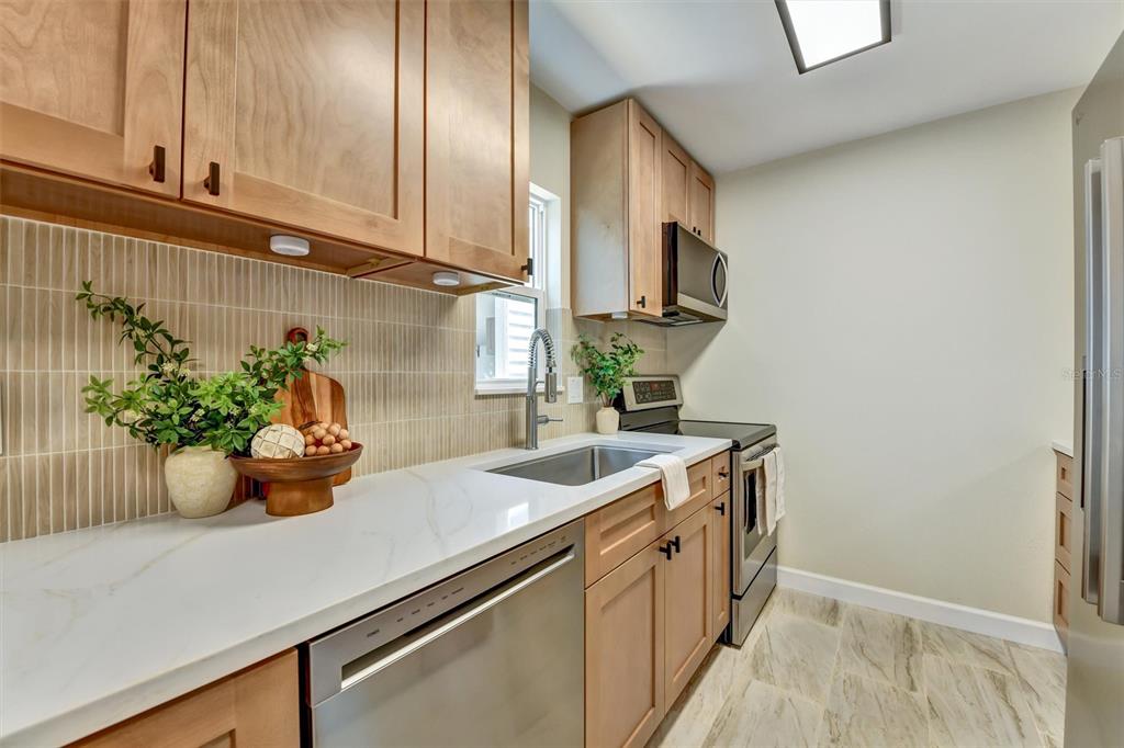 A kitchen features light wood cabinets, white countertops, stainless steel appliances, and a tiled backsplash — 11906 DIETZ DRIVE UNIT 22, TAMPA, FL