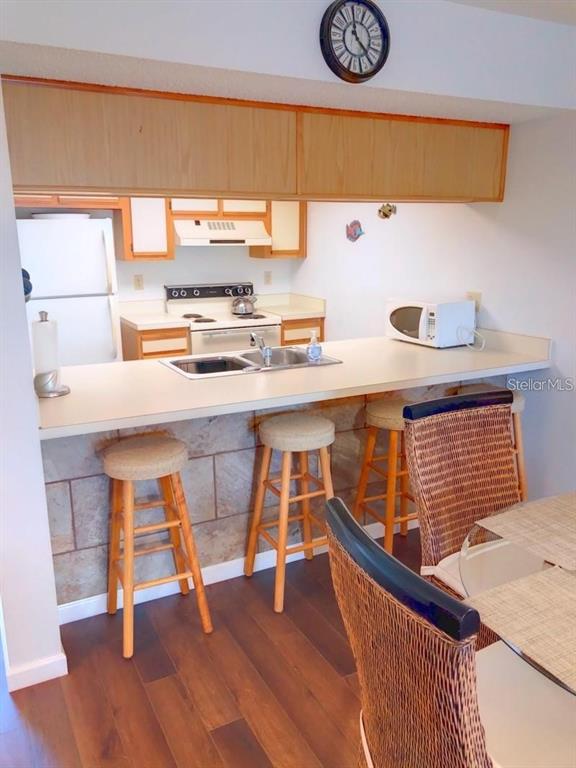 A kitchen features a breakfast bar with three stools, light wood cabinets, and tile backsplash — 4056 OAKVIEW DRIVE UNIT E7, PORT CHARLOTTE, FL