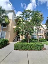 A multi-story tan apartment building features a central staircase, balconies, and a landscaped front yard — 3190 DANTE DRIVE UNIT 102, ORLANDO, FL