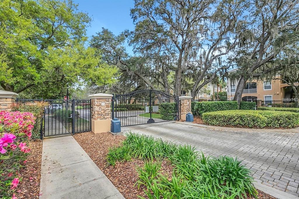 A gated entrance with stone pillars, wrought iron gates, and mature trees in a residential area — 3190 DANTE DRIVE UNIT 102, ORLANDO, FL