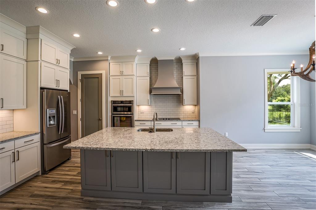 A modern kitchen features white cabinetry, a gray island with a granite countertop, and stainless appliances — LOT H-19 ISLAND CLUB DRIVE, TAVARES, FL