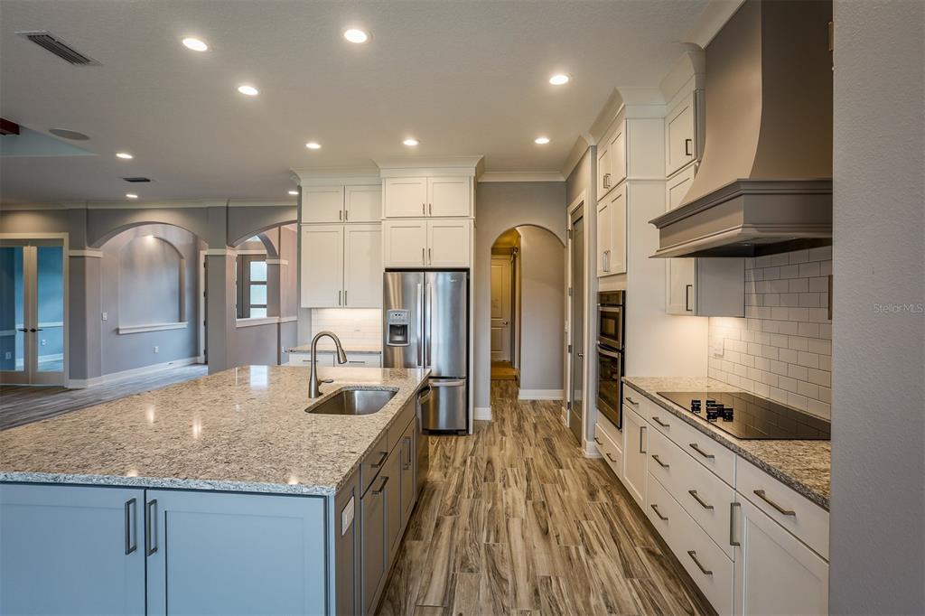 A modern kitchen features white cabinetry, granite countertops, a large island, and stainless steel appliances — LOT H-19 ISLAND CLUB DRIVE, TAVARES, FL