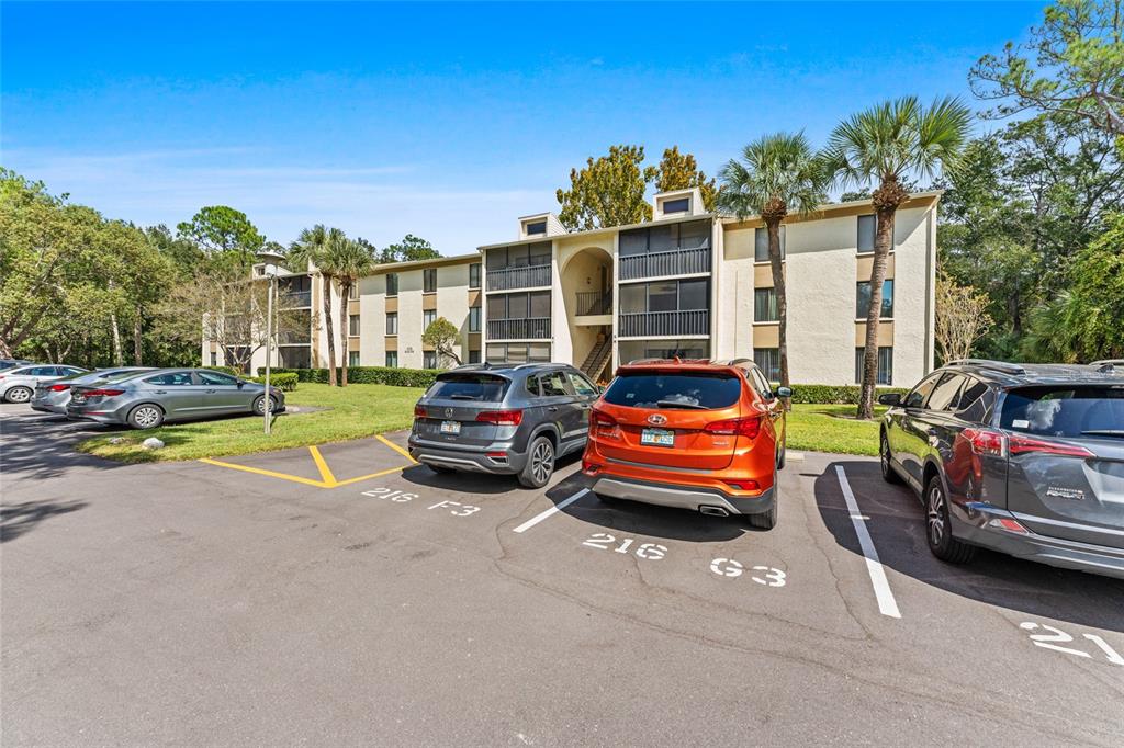 A three-story apartment building stands behind a parking lot with several parked cars — 3232 LAKE PINE WAY E UNIT F2, TARPON SPRINGS, FL