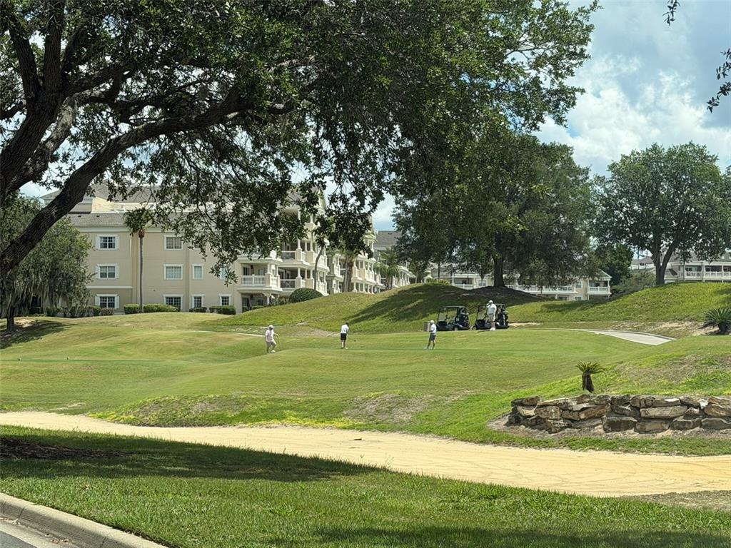 A golf course green with three golfers and two golf carts near a large building — 7656 WHISPER WAY UNIT 401, REUNION, FL