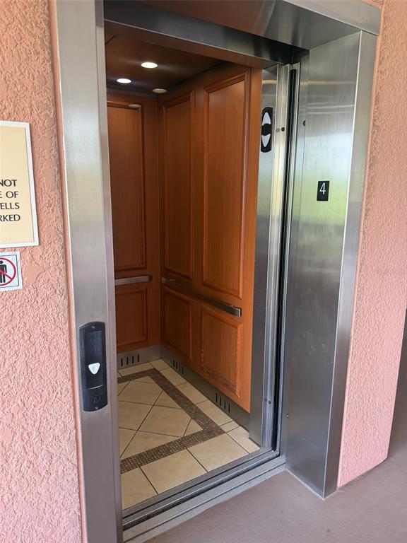 An elevator with wood-paneled walls and a tiled floor opens onto a pink stucco hallway — 7656 WHISPER WAY UNIT 401, REUNION, FL