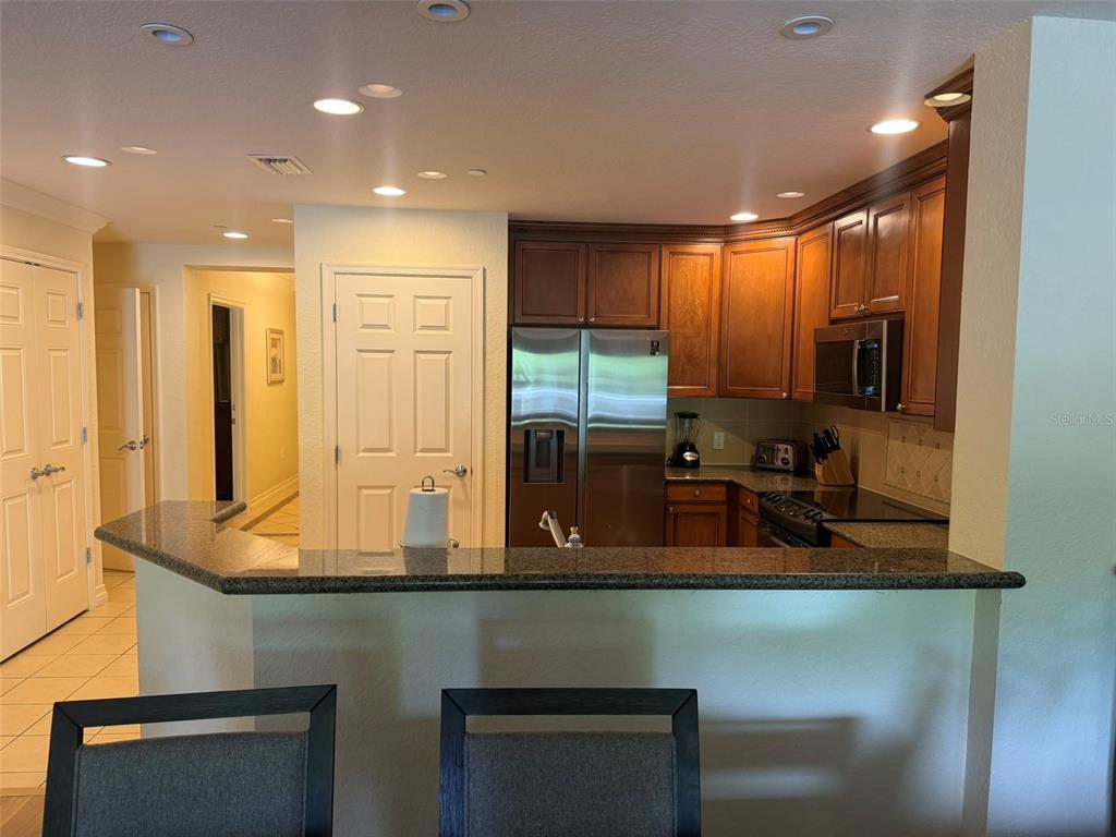 A kitchen features dark wood cabinets, stainless steel appliances, and a granite-topped breakfast bar — 7656 WHISPER WAY UNIT 401, REUNION, FL