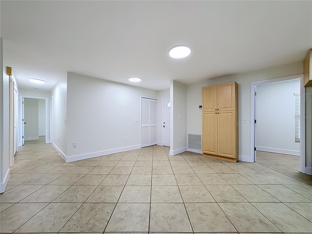 A room with light-colored tile flooring, white walls, a wooden cabinet, and multiple doorways — 2103 162ND STREET E, BRADENTON, FL