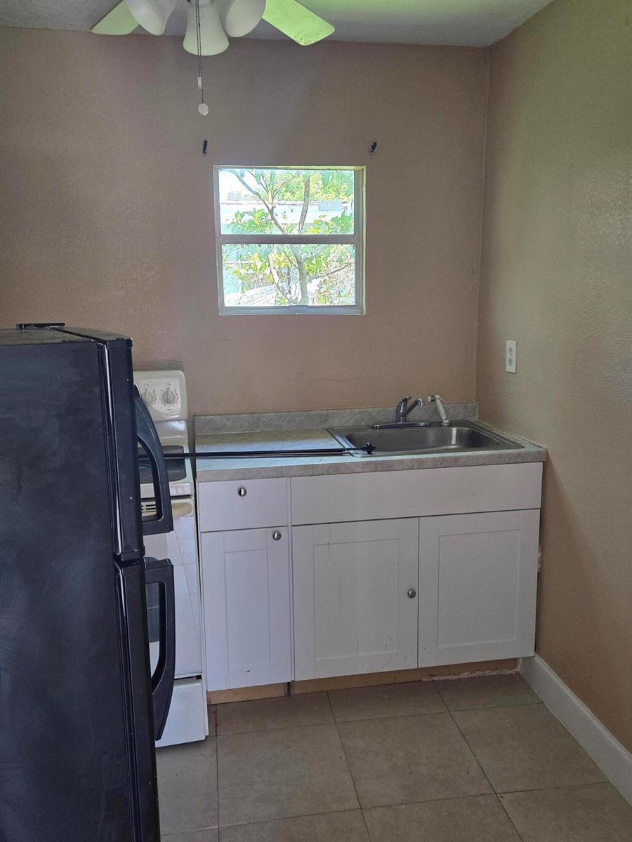 A small kitchen features a black refrigerator, a white stove, a sink, and white cabinets — 815 Silver Beach Road # B, Lake Park FL 33403, LAKE PARK, FL