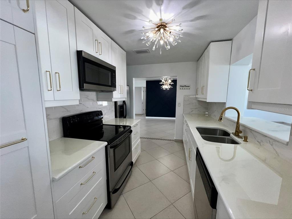 A galley kitchen features white cabinets, marble-look countertops, stainless steel appliances, and a modern chandelier — 1211 LEHIGH STREET, KISSIMMEE, FL
