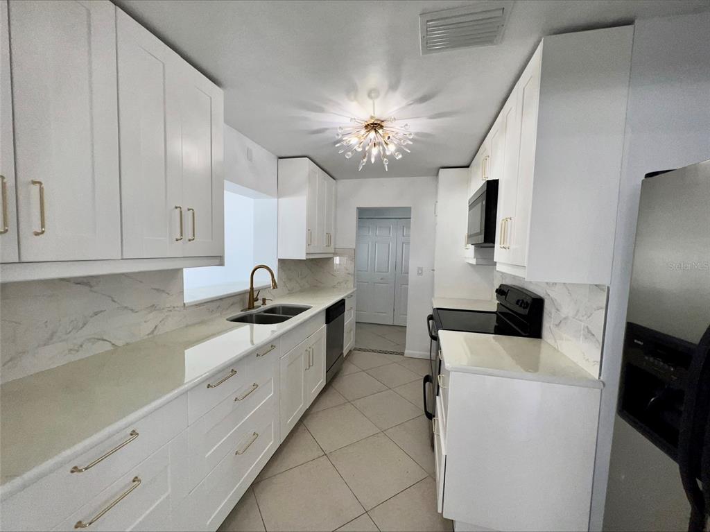 A galley kitchen features white cabinets, quartz countertops, stainless steel appliances, and a modern chandelier — 1211 LEHIGH STREET, KISSIMMEE, FL