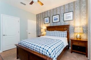 A bedroom features a wooden bed with a plaid comforter against a patterned accent wall — 2959 BANANA PALM DRIVE, KISSIMMEE, FL