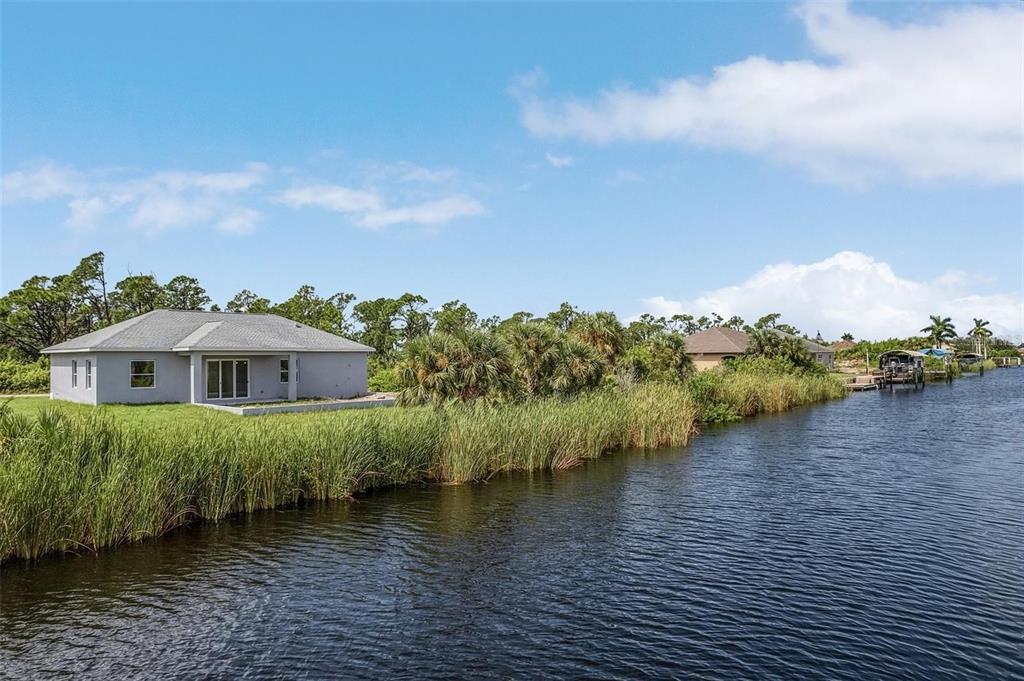 A gray house sits on a grassy bank next to a canal with tall reeds — 14292 KAY LANE, PORT CHARLOTTE, FL