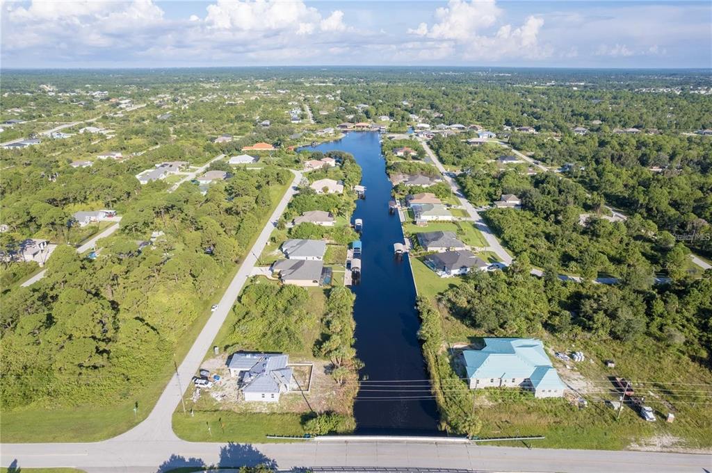 An aerial view shows a canal lined with houses and trees under a blue sky — 14292 KAY LANE, PORT CHARLOTTE, FL