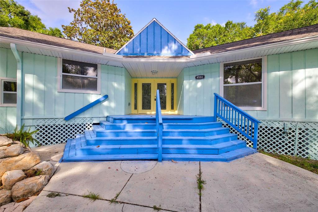 A light blue house features a bright yellow double door and a wide blue staircase — 4586 S FLAMBEAU LOOP, HOMOSASSA, FL