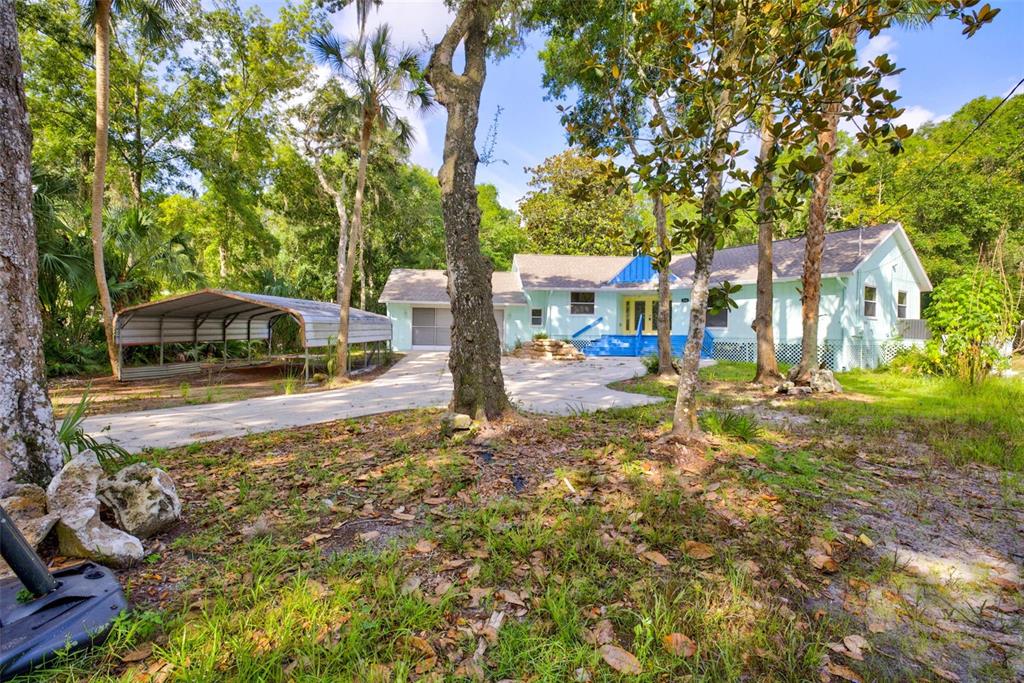 A light blue house with a metal carport sits on a wooded lot with trees — 4586 S FLAMBEAU LOOP, HOMOSASSA, FL