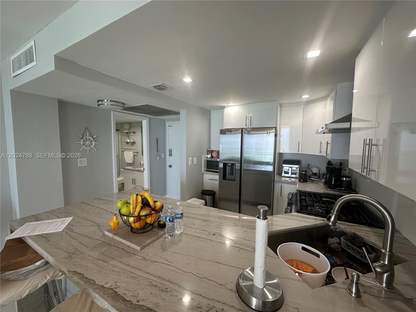 A kitchen features a stone-topped island, stainless steel appliances, and white cabinetry — 2030 S Ocean Dr # 916, Hallandale Beach FL 33009, HALLANDALE BEACH, FL