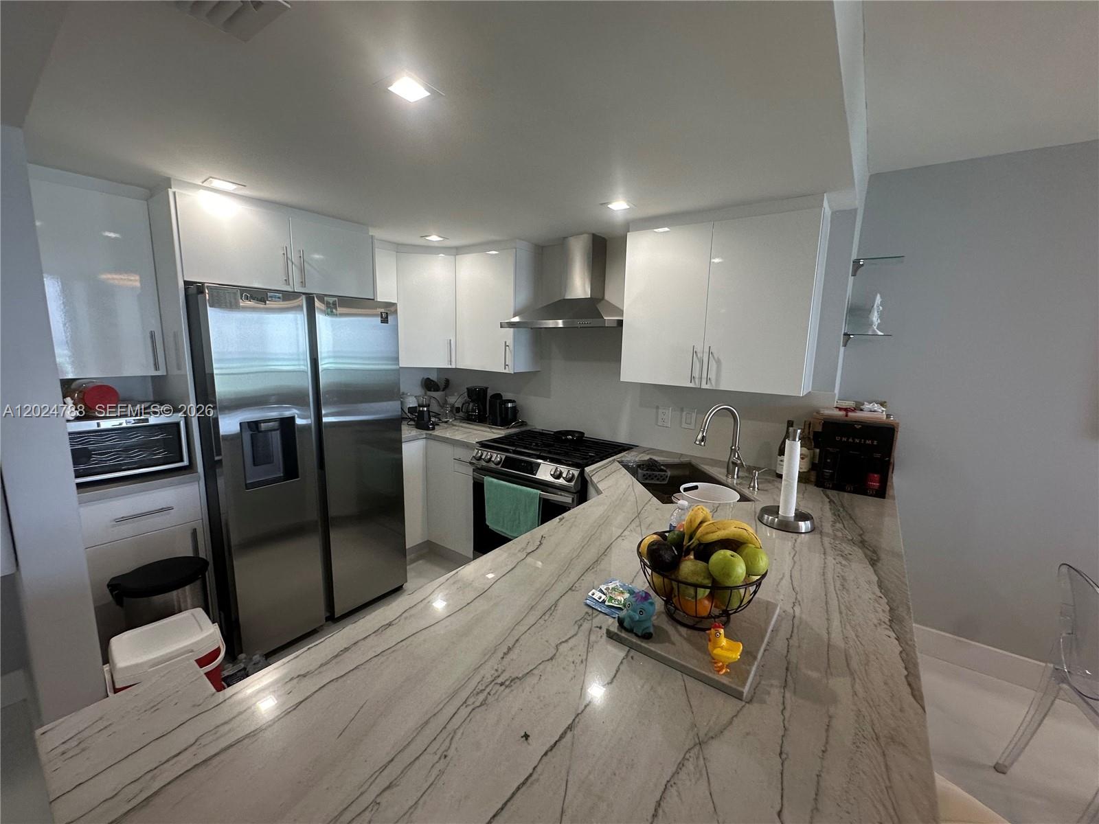 A modern kitchen features white cabinets, stainless steel appliances, and a large stone countertop — 2030 S Ocean Dr # 916, Hallandale Beach FL 33009, HALLANDALE BEACH, FL