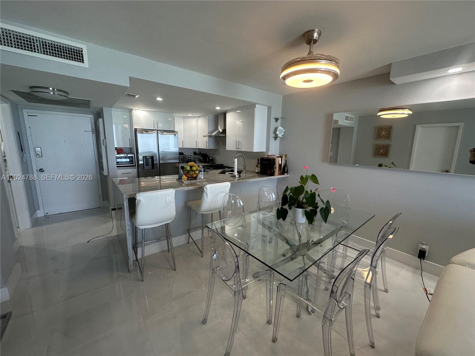 A modern kitchen and dining area feature white cabinetry, a glass table, and transparent chairs — 2030 S Ocean Dr # 916, Hallandale Beach FL 33009, HALLANDALE BEACH, FL
