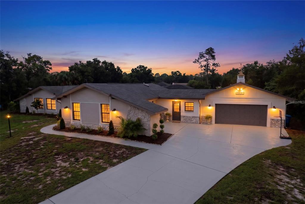An exterior view of a single-story house with a garage and a concrete driveway at dusk — 7231 RIVER COUNTRY DRIVE, WEEKI WACHEE, FL