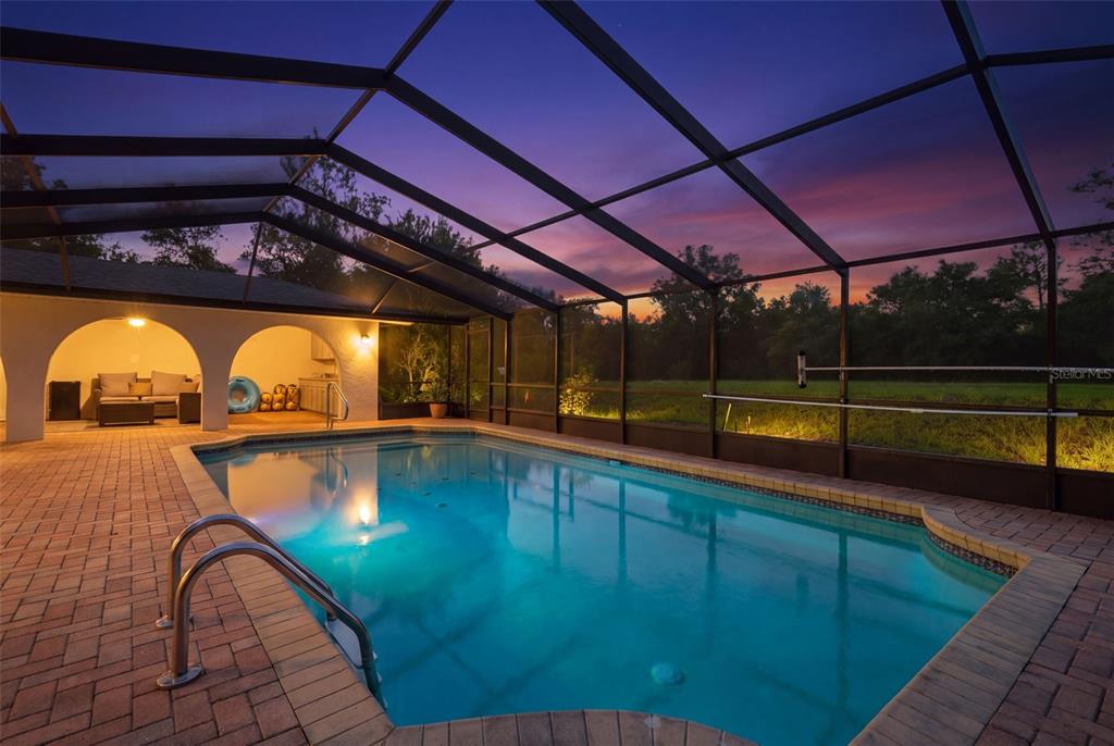 A screened-in swimming pool with a brick patio and a covered seating area at sunset — 7231 RIVER COUNTRY DRIVE, WEEKI WACHEE, FL