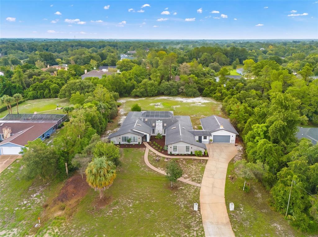 An aerial view shows a single-story house with a solar-paneled roof and a long driveway — 7231 RIVER COUNTRY DRIVE, WEEKI WACHEE, FL