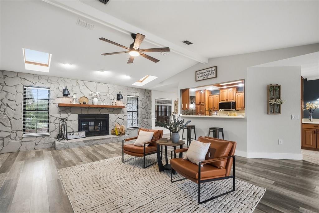 A living room features a stone fireplace, wood-look flooring, and an open view into the kitchen — 7231 RIVER COUNTRY DRIVE, WEEKI WACHEE, FL
