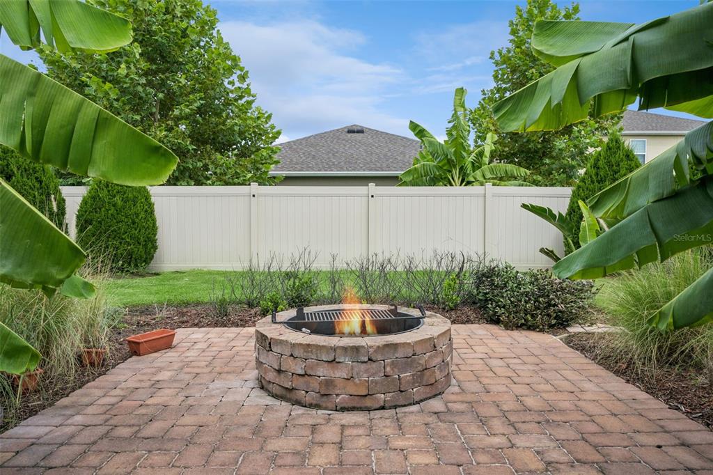 A stone fire pit sits on a brick patio in a backyard with a privacy fence — 1055 CHASE AUSTIN WAY, SANFORD, FL