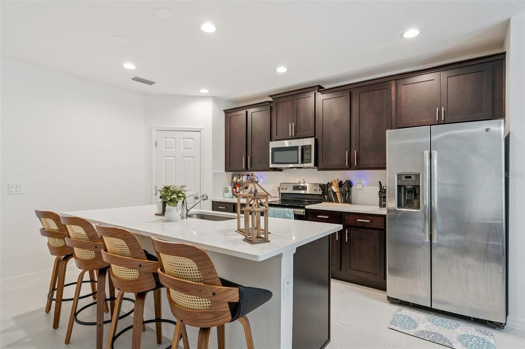 A kitchen features dark wood cabinets, stainless steel appliances, a white island, and three barstools — 1055 CHASE AUSTIN WAY, SANFORD, FL