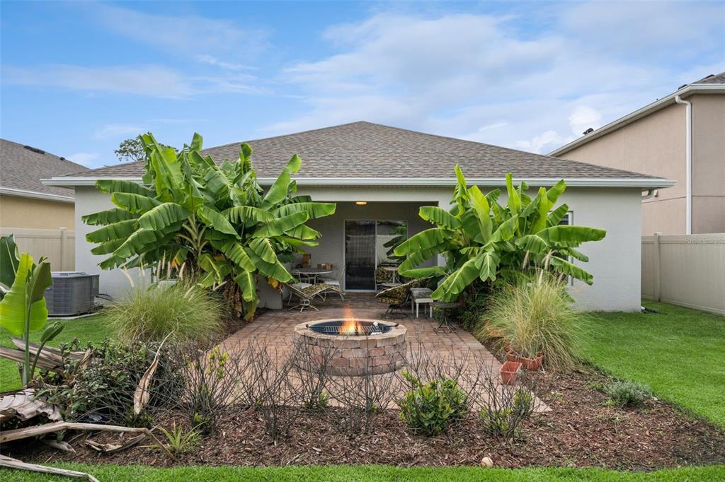 A backyard patio features a stone fire pit, banana trees, and a covered porch area — 1055 CHASE AUSTIN WAY, SANFORD, FL