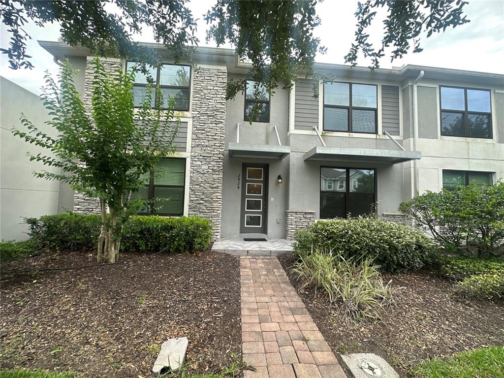A two-story townhouse exterior features a stone facade, a brick walkway, and a front door — 2928 WINDMILL DRIVE, KISSIMMEE, FL