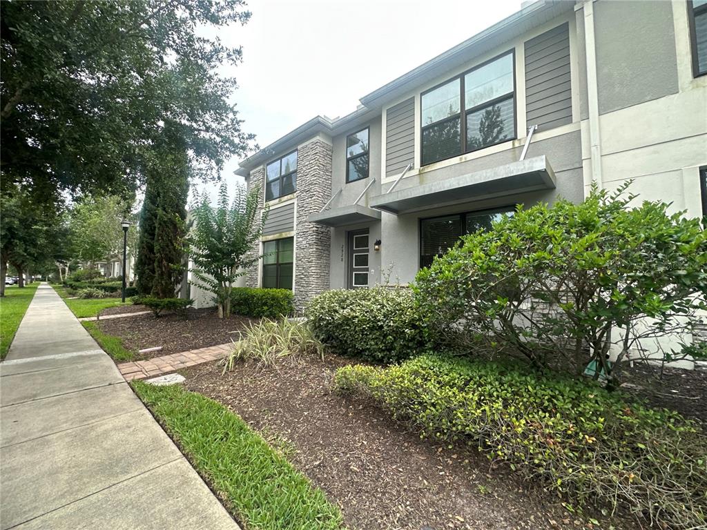 A two-story townhouse exterior features stone veneer, gray siding, and a landscaped front yard — 2928 WINDMILL DRIVE, KISSIMMEE, FL