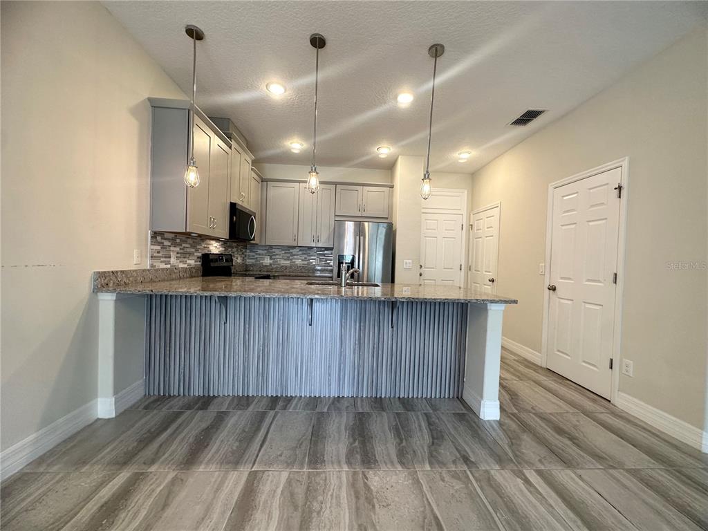 A kitchen features gray cabinets, granite countertops, a slatted breakfast bar, and wood-look tile flooring — 2928 WINDMILL DRIVE, KISSIMMEE, FL