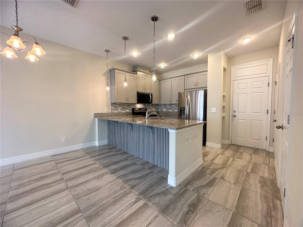 A kitchen features light gray cabinets, granite countertops, a breakfast bar, and wood-look tile flooring — 2928 WINDMILL DRIVE, KISSIMMEE, FL