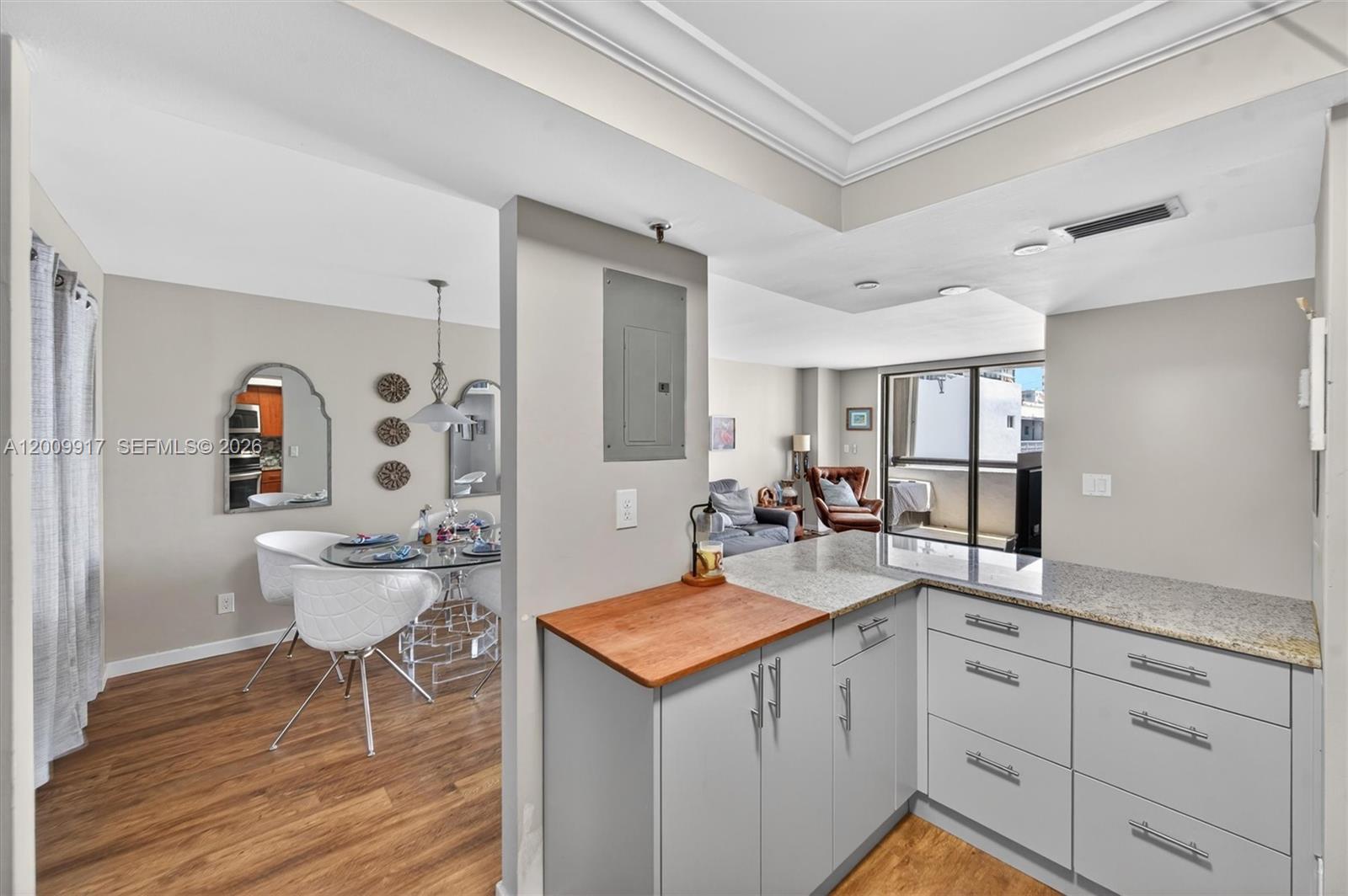 A kitchen with gray cabinets and granite countertops overlooks a dining area and living room — 1775 Washington Ave # 7B, Miami Beach FL 33139, MIAMI BEACH, FL