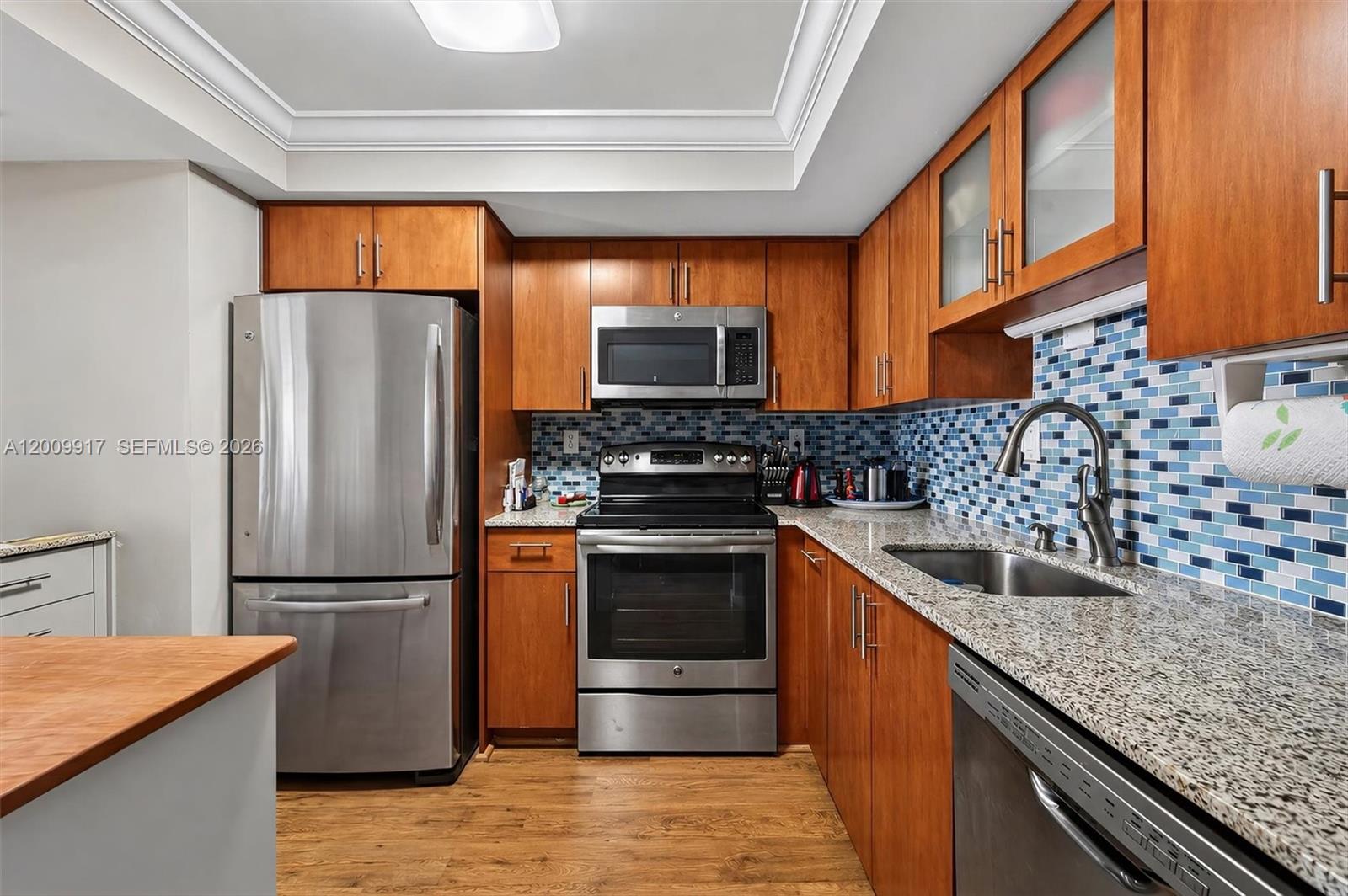 A kitchen features wood cabinets, stainless steel appliances, granite countertops, and a blue mosaic backsplash — 1775 Washington Ave # 7B, Miami Beach FL 33139, MIAMI BEACH, FL